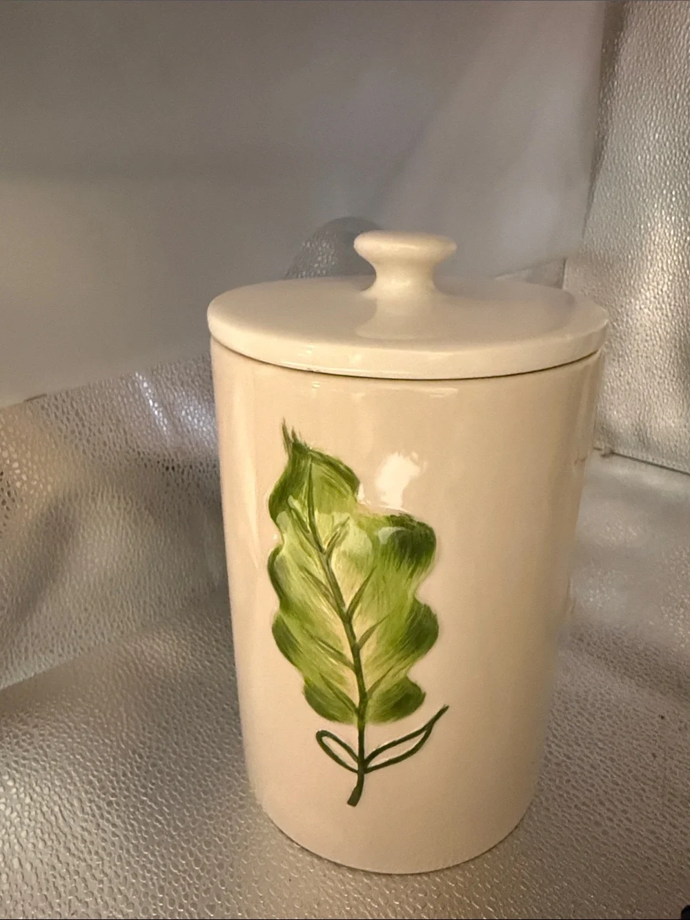Vintage cylindrical Pier 1 cream canister with a hand painted green leaf
